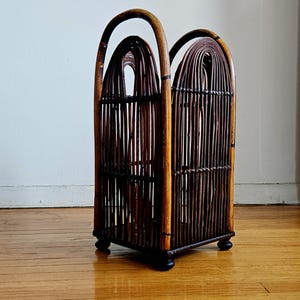 May include: A brown bamboo umbrella stand with a square base and arched sides. The stand has a woven design and is made of natural materials.