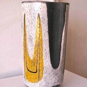 May include: A cylindrical ceramic vase featuring a speckled white and black finish. The exterior is decorated with a prominent, vertical yellow U-shaped graphic outlined in thin black lines, contrasted by a large, solid dark gray vertical panel.