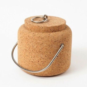 Puede incluir: Un recipiente de corcho con un asa de metal y una tapa de corcho con un anillo de metal. El recipiente es marr&oacute;n y tiene una textura rugosa.