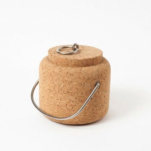 Puede incluir: Un recipiente de corcho con un asa de metal y un anillo de metal en la tapa. El recipiente est&aacute; hecho de corcho natural y tiene un color marr&oacute;n claro.