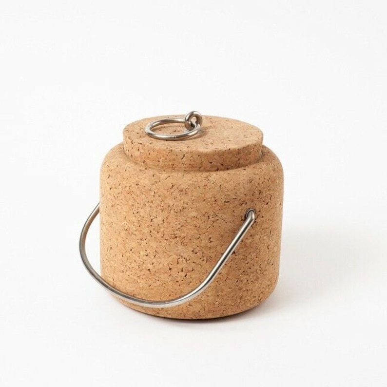 Puede incluir: Un recipiente de corcho con un asa de metal y un anillo de metal en la tapa. El recipiente est&aacute; hecho de corcho natural y tiene un color marr&oacute;n claro.