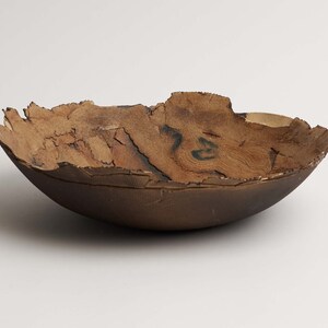 May include: A handcrafted, brown ceramic bowl with a unique, textured rim. The bowl's interior features a natural wood grain pattern, adding a rustic aesthetic. The bowl is approximately 25 cm in diameter and 10 cm deep.