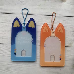 May include: Two plastic card holders with a cat-shaped design. The holder on the left is blue with the text "Love you because" and the holder on the right is orange.
