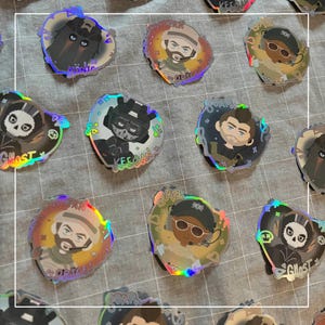 Könnte beinhalten: Eine Sammlung holografischer Aufkleber mit verschiedenen Charakterdesigns. Die Aufkleber zeigen Charaktere mit Namen wie "Ghost", "König", "Captain", "Gaz" und "Soap". Jeder Aufkleber hat ein einzigartiges Design und Farbschema mit einem glänzenden, irisierenden Finish.