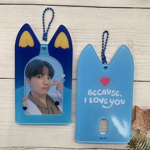 May include: Two blue and white cat-shaped keychains with a chain attached. One keychain has a photo frame with a picture of a young man inside. The other keychain has the text "Because, I love you" printed on it.