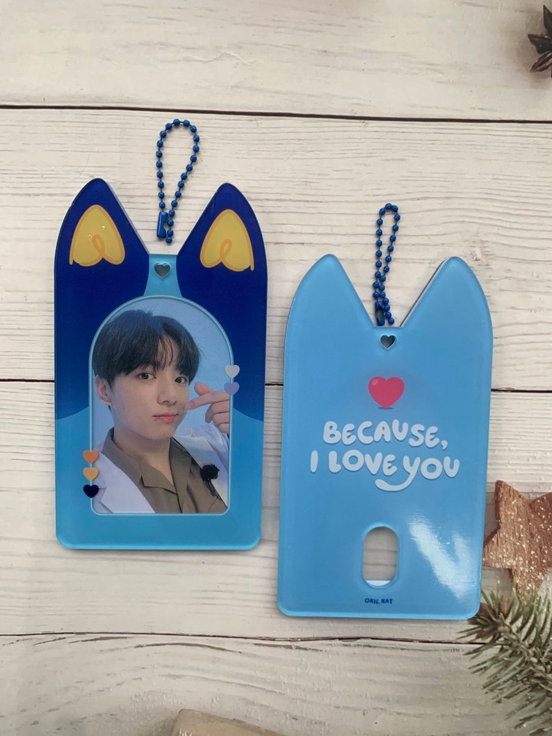 May include: Two blue and white cat-shaped keychains with a chain attached. One keychain has a photo frame with a picture of a young man inside. The other keychain has the text "Because, I love you" printed on it.