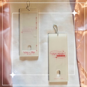 Peut inclure: Deux porte-clés rectangulaires en plastique transparent avec des attaches à chaîne argentée. L'un porte l'inscription "You + Me 4EVER" en rose, l'autre "Girl Math" en rose. Les deux ont une petite découpe rectangulaire en bas.