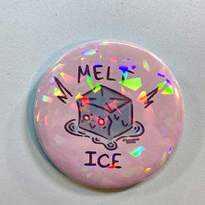 May include: A circular pin-back button with a light pink background and a holographic finish. The design features a cartoon blue ice cube melting into a puddle with the text MELT ICE printed in black above and below the illustration.