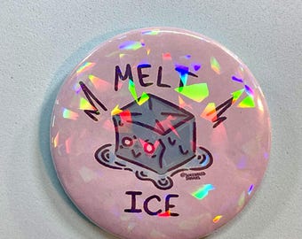 May include: A circular pin-back button with a light pink background and a holographic finish. The design features a cartoon blue ice cube melting into a puddle with the text MELT ICE printed in black above and below the illustration.