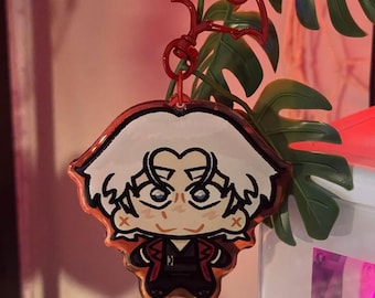 May include: An acrylic keychain featuring a stylized cartoon character with white hair, blue eyes, and a red and black outfit. The keychain is attached to a red bat-shaped clasp, creating a distinct accessory with a glossy finish and clear edges.