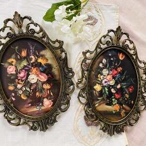 May include: Two ornate gold oval frames with intricate details, each holding a floral print with a bouquet of colorful flowers in a vase.