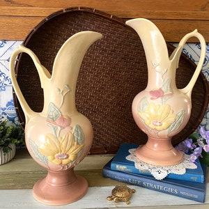 May include: Two vintage ceramic pitchers with floral designs in shades of pink, yellow, and green. The pitchers have a delicate, feminine aesthetic and are perfect for adding a touch of vintage charm to any home.