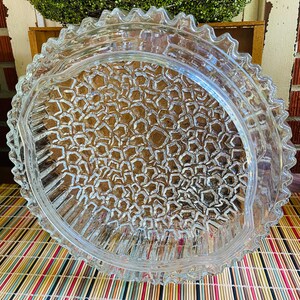 May include: A clear glass serving dish with a scalloped edge and a textured bottom. The dish is made of thick glass and has a vintage look.