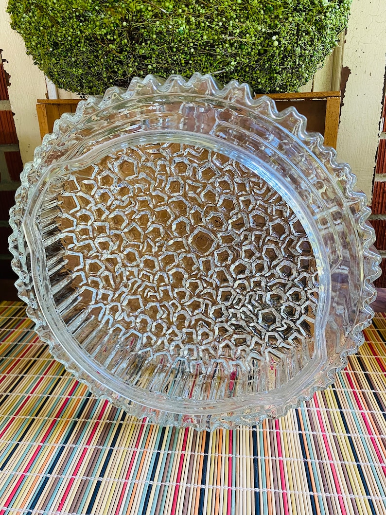 May include: A clear glass serving dish with a scalloped edge and a textured bottom. The dish is made of thick glass and has a vintage look.