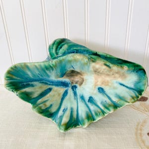 May include: A ceramic bowl with a green, blue, and white glaze. The bowl is shaped like a seashell and has a wavy, organic design.