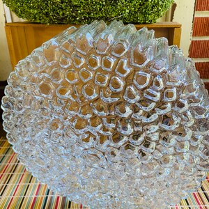 May include: A clear glass ceiling light fitting with a textured, honeycomb-like design. The light fitting is round and has a diameter of approximately 30 cm.