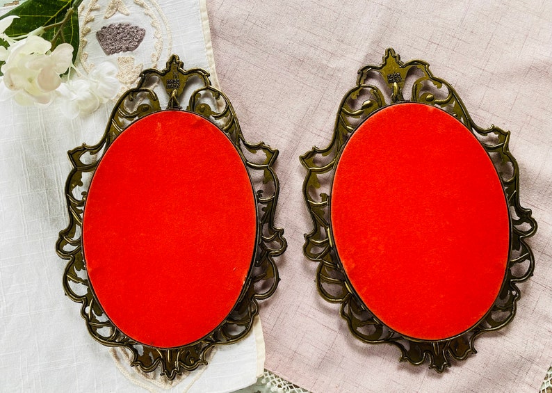 May include: Two ornate gold-colored picture frames with red velvet backing. The frames have a detailed, intricate design.