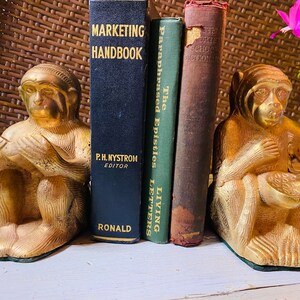 May include: A pair of gold monkey bookends holding books titled "The Paraphrased Epistles & Living Letters" and "Marketing Handbook".