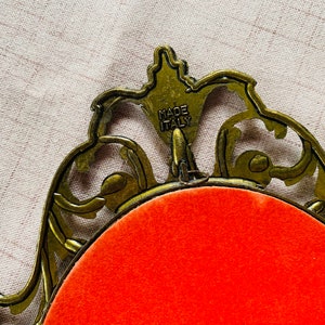 May include: A gold-colored ornate picture frame with a red velvet backing. The frame is made in Italy.