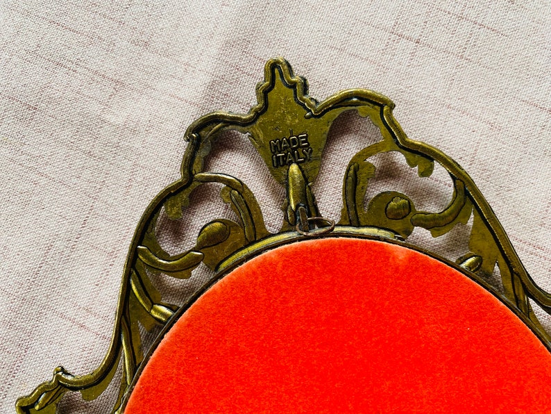 May include: A gold-colored ornate picture frame with a red velvet backing. The frame is made in Italy.