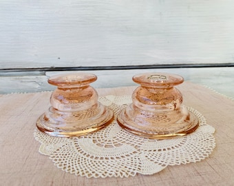 May include: Two pink glass candle holders with a textured design. The candle holders are sitting on a white crocheted doily.