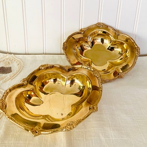 May include: Two gold-tone metal serving dishes with ornate edges. The dishes are shaped like a clover leaf and have a shiny finish.