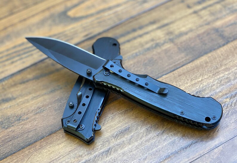 May include: A black folding knife with a black handle and a partially serrated blade. The knife has a pocket clip and a textured handle.
