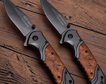 May include: Two folding pocket knives with dark grey metal blades and handles featuring wood grain inlays. The left blade is engraved with BEST MAN 11.10.2026 and the handle with Justin. The right blade reads GROOMSMAN 11.10.2026 and the handle Steve.