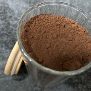 Puede incluir: Un tarro de vidrio lleno de un polvo marrón, probablemente cacao en polvo o polvo de chocolate.