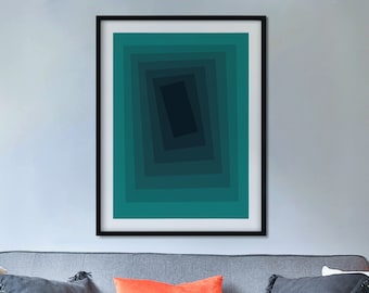May include: A gray couch with pillows in various colors and textures, including white, gray, and orange. A framed abstract art print with a teal and black design hangs above the couch. A small glass vase with a green plant sits on a coffee table in front of the couch.