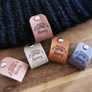 May include: Five leather tags with a rainbow and the text "THIS BELONGS TO Henry" in brown lettering. The tags are in various colours: brown, tan, grey, and orange.