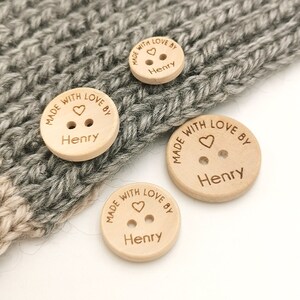May include: Three wooden buttons with the text "Made with love by Henry" and a small heart symbol. The buttons are different sizes and are on a white background.