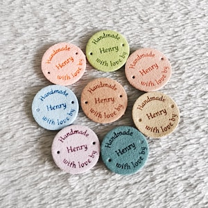 May include: Nine round leather labels with holes for sewing. Each label is a different pastel colour and has the text "Handmade Henry with love by" in a handwritten font.
