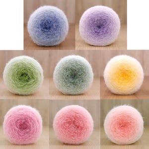 May include: Seven balls of yarn in a range of colours, including blue, purple, green, yellow, pink, and peach. Each ball features a gradient effect, transitioning between shades. The yarn appears soft and fluffy, ideal for knitting or crochet projects.