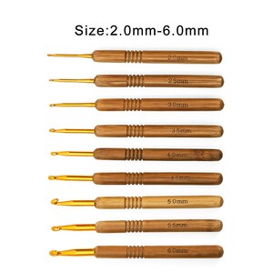 Puede incluir: Un juego de nueve ganchillos con mangos de madera y puntas de metal dorado. Los tama&ntilde;os var&iacute;an de 2,0 mm a 6,0 mm, con cada tama&ntilde;o claramente etiquetado en el mango. Los mangos son de color marr&oacute;n claro.