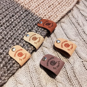 May include: Five leather tags with the text "Handmade by Henry" and a small image of a ball of yarn. The tags are in different colours: brown, beige, grey, and tan.