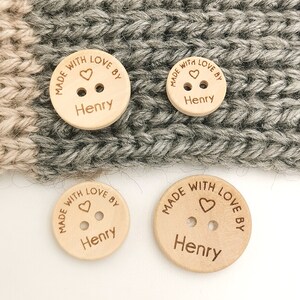 May include: Three wooden buttons with the text "Made with love by Henry" and a small heart design. The buttons are on a gray knitted fabric background.