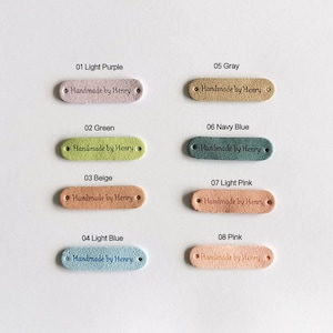 Peut inclure: Huit &eacute;tiquettes en cuir ovales de diff&eacute;rentes couleurs, chacune avec le texte "Handmade by Henry" dans une police d'&eacute;criture manuscrite.