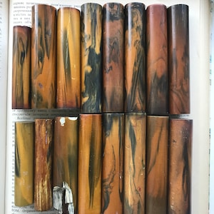 Peut inclure: Une collection de 12  blancs de stylo marbrés brun et noir. Les blancs sont cylindriques et ont une finition lisse et polie.