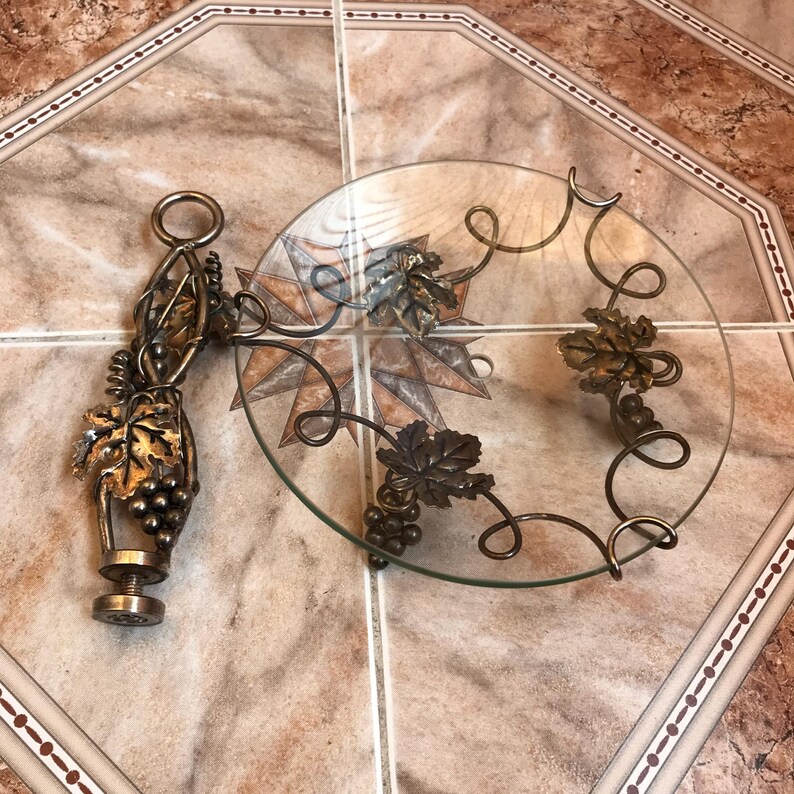 May include: A glass serving tray with a metal base featuring a grapevine design. The base is decorated with gold-colored leaves and grapes.