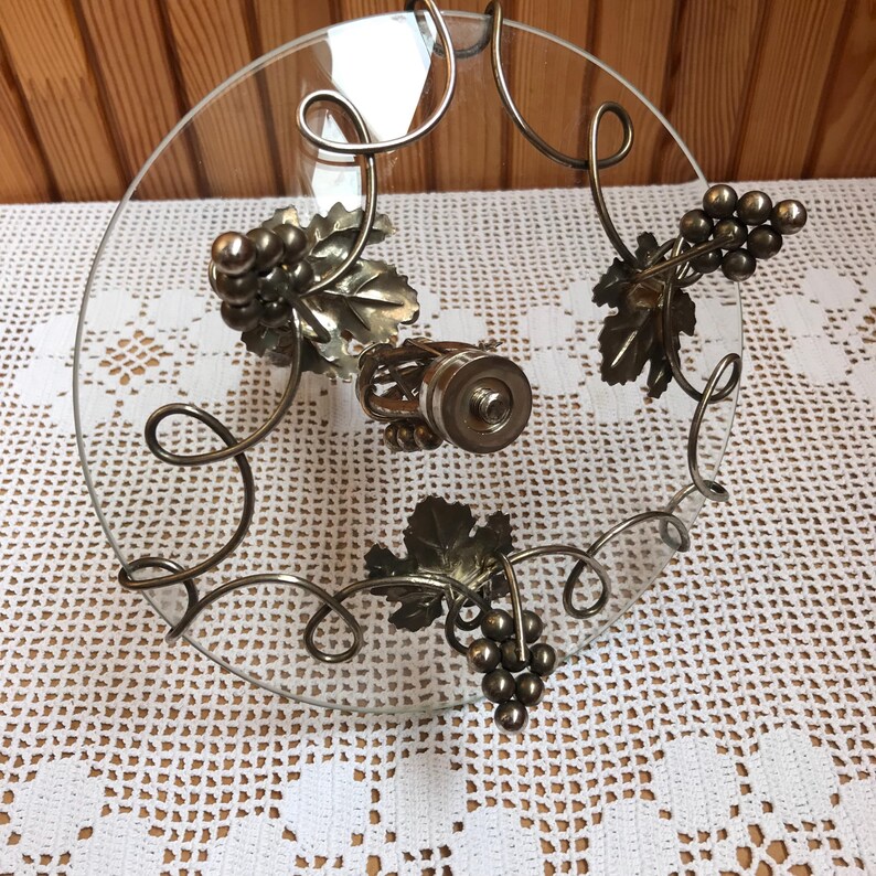 May include: A glass serving tray with a metal grapevine design. The tray has three grape clusters and leaves, and a metal knob in the center.