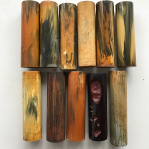 May include: Twelve cylindrical pieces of wood with various patterns and colours, including brown, black, yellow, and orange. The wood pieces are arranged in two rows of six.