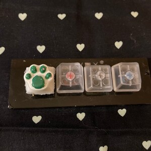 Könnte beinhalten: Vier Tastenkappen für eine mechanische Tastatur. Die Tastenkappen sind transparent und haben einen schwarzen Hintergrund. Die Tastenkappen sind mit den Buchstaben "E", "R", "T" und "Y" beschriftet. Die Tastenkappen sind von einem schwarzen Rahmen umgeben. Die Tastenkappen befinden sich auf einer schwarzen Oberfläche.