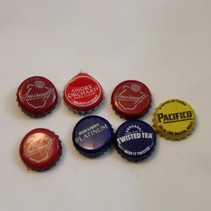 May include: A collection of seven bottle caps, each with a different brand logo and design. The caps are red, blue, yellow, and white.