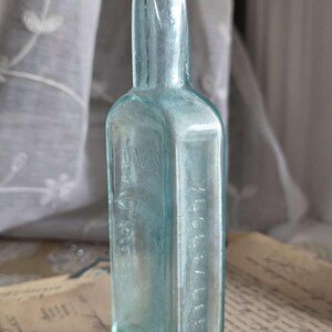 May include: A vintage, rectangular, light blue glass bottle. The bottle has a narrow neck and a slightly rounded shoulder. The text "DAVIS" is embossed on the front, and "VICHELLE" is embossed on the side. The bottle is displayed on a vintage paper.