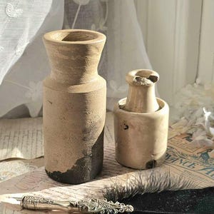 Puede incluir: Dos tinteros de cerámica vintage, uno con base negra, y una pluma de pluma negra sobre una hoja de papel antiguo.