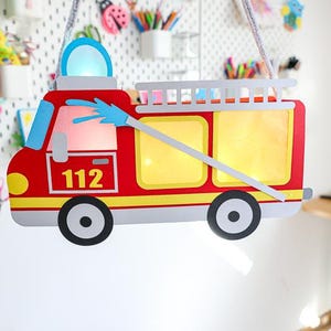以下が含まれることがあります： 青い放水ホースと番号112が付いた、赤と黄色の消防車型のランタン。 ランタンの上部には梯子があり、灰色の紐から吊り下げられています。 窓は黄色で照らされています。