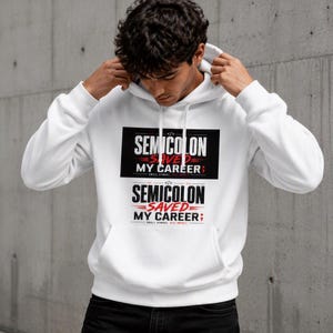 Op de afbeelding: Een wit sweatshirt met capuchon en lange mouwen met een grafische print op de borst. Het ontwerp bevat de tekst "SEMICOLON SAVED MY CAREER" in zwarte en rode letters, vergezeld van een puntkomma-symbool en de zin "SMALL SYMBOL BIG IMPACT."