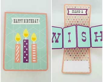 May include: A teal and orange card with a pop-up that says "make a wish". The front of the card has a happy birthday message and three candles with yellow flames.