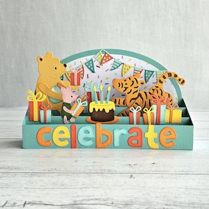 May include: A layered papercraft birthday card featuring a yellow bear, a pink pig, and a tiger. The card includes a birthday cake with candles, wrapped gifts, and the word "celebrate" in colorful letters.